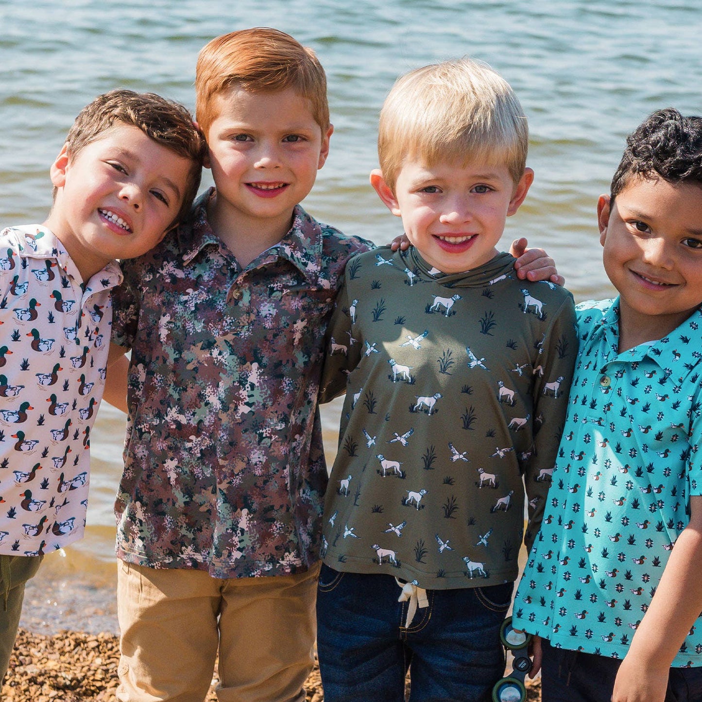 Four children standing together on a beach, wearing patterned shirts and boots.